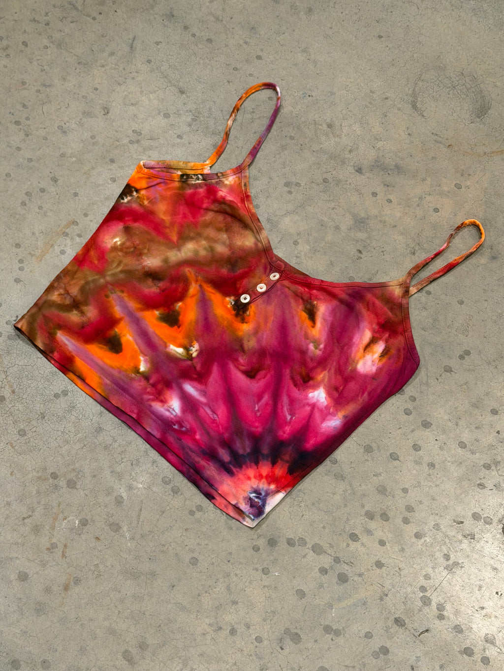 Hand-dyed crop tank top with flame pattern in magenta, orange, and purple tones, laid flat on concrete